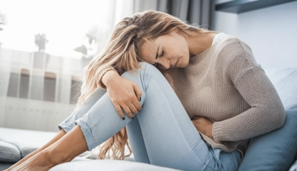 Femme assise, douleur abdominale visible.